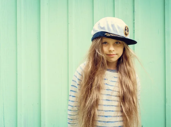Sevimli küçük kız denizci şapkası ve alan metin için gülümseyen bir turkuaz duvarının yakınında standları. — Stok fotoğraf