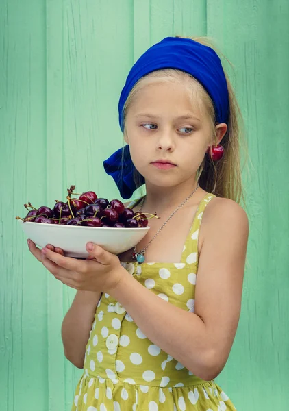 Hermosa chica rubia sobre un fondo de pared de color turquesa placa de retención con cereza . — Foto de Stock