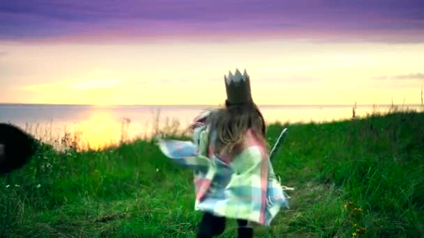 Girl with boy dressed as kings run on the field next to the sea — Stock Video