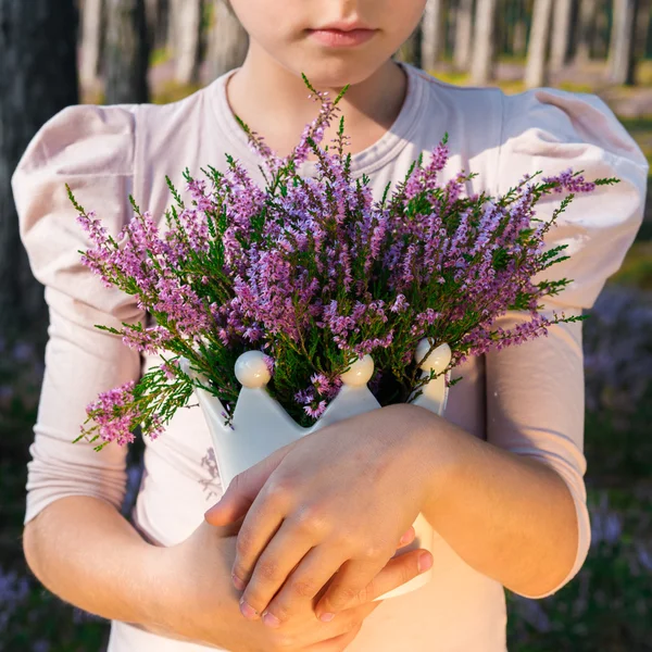 Hermosa chica en el bosque sosteniendo en un jarrón con brezo . — Foto de Stock