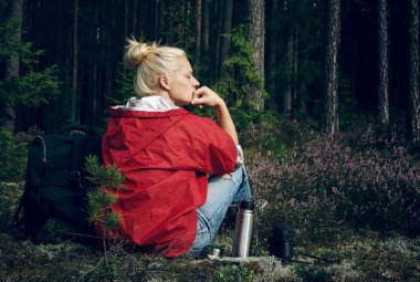 Young active woman tourist sitting in a clearing in the forest and looking at the forest.Healthy active lifestyle concept.
