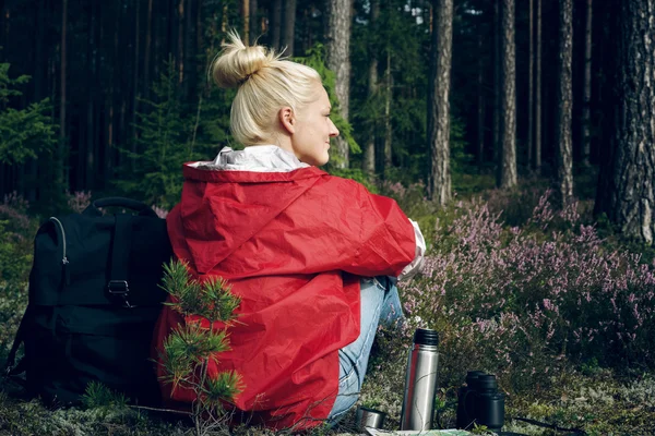 Young active woman tourist sitting in a clearing in the forest and looking at the forest.Healthy active lifestyle concept. — Stock Fotó