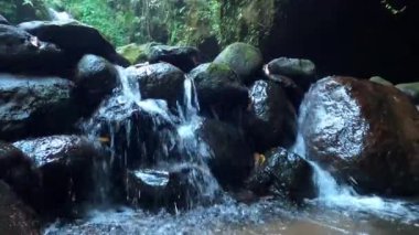 Kayalardaki boşluklar arasındaki nehrin dingin akışını gösteren doğal nehir kayalarıyla dolu küçük bir şelale. Gökyüzü kararmaya başladığında Endonezya 'daki nehir akıntısının hareketi..