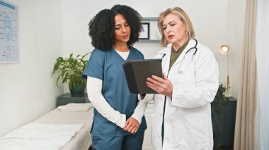 İki sağlık uzmanı, hasta odaklı bir ortamda takım çalışması, bakım ve profesyonel tıbbi işbirliğinin vurgulandığı temiz bir klinikteki bir panoda bilgileri gözden geçirirler..