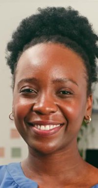 Doğal kıvırcık saçlı güzel bir Afrikalı Amerikalı kadın kameraya parlak ve samimi bir şekilde gülümsüyor. Işıl ışıl ifadesi, bu yakın portrede neşe, güven ve pozitif duygu aktarıyor..