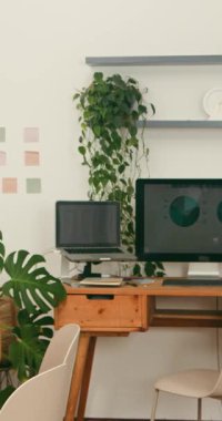 Ahşap bir masa, verileri gösteren çift monitörler ve yemyeşil bitkilerin yer aldığı davetkâr bir ofis kurulumu. Uzaktan çalışmayı, verimliliği veya sakin bir profesyonel çevreyi resmetmek için mükemmel..