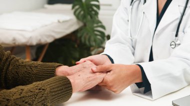 Beyaz önlüklü bir doktor yaşlı bir hastanın elini nazikçe tutar ve tıbbi bir ortamda empati, güven ve kişisel bakım sağlar..