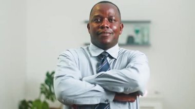 Parlak, modern ofis ortamında kollarını kavuşturarak gülümseyen kendinden emin bir Afro-Amerikan işadamının portresi. Bu video profesyonelliği, başarıyı ve ulaşılabilirliği aktarır..