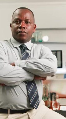 Kollarını kavuşturmuş özgüvenli bir Afro-Amerikan işadamı modern bir şirket ofisinde poz veriyor. Ciddi ve kararlı ifadesi, iş yerinde güçlü bir liderlik ve profesyonel odaklanmayı yansıtıyor..