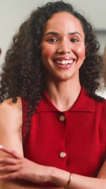 Kendine güvenen kıvırcık saçlı genç bir iş kadını kameraya parlak bir şekilde gülümser ve kollarını profesyonel bir ortamda kavuşturur. Olumlu ve başarılı olduğunu gösteriyor..