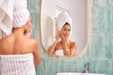 Kafasına havlu sarılmış bir kadının, yeşil fayanslarla çevrili yuvarlak bir aynaya yansıyan şık bir banyoda cilt bakımı yaptığı rahat bir an..