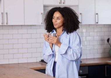 Parlak bir mutfakta mavi çizgili gömleği olan şık bir kadın fincandan yudumluyor. Bu rahat, rahat an günlük hayatı, rahatlığı ve ev sıcaklığını yakalar..