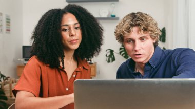 İki genç profesyonel, parlak ve modern bir ofiste dizüstü bilgisayarda birlikte çalışıyorlar. Sahne, üretken ve işbirlikçi bir ortamda takım çalışması, işbirliği ve başlangıç enerjisi taşır.