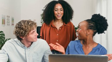 Parlak bir ofisteki üç farklı iş arkadaşı fikirleri ve gülümsemeleri paylaşıyor, takım çalışmasını, yaratıcılığı ve dizüstü bilgisayarın etrafında destekleyici bir başlangıç titreşimini vurguluyorlar..