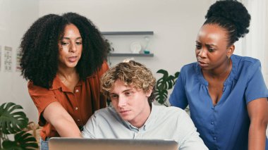 Üç farklı profesyonel, parlak bir ofiste dizüstü bilgisayarın etrafında toplanarak fikirler ve planlama üzerinde işbirliği yapıyorlar. İfadeleri, başlangıç ortamında odaklanma, takım çalışması ve yaratıcı enerjiyi gösteriyor..