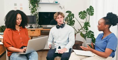 Dizüstü bilgisayarlar üzerinde çalışırken, notlar alırken ve fikirleri paylaşırken, parlak, sıradan bir ofis sohbetinde üç takım arkadaşı. Çeşitli bir grup, modern bir çalışma alanında işbirliğini, yaratıcılığı ve verimli tartışmaları teşvik eder..