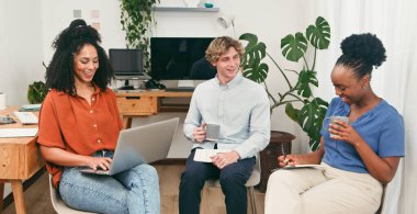 Üç iş arkadaşı, bitkilerle dolu parlak bir ofiste rahat ve üretken bir anı paylaşıyor. Beyin fırtınası yapmak ve işbirliği yapmak için dizüstü bilgisayar kullanırken sohbet eder, notlar alır ve kahveden zevk alırlar..