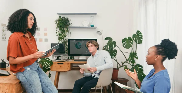 Üç meslektaş parlak, bitki dolu bir ofiste fikirleri tartışıyor. Dizüstü bilgisayarlar, not defterleri ve takım çalışmasını ve yaratıcı problem çözmeyi yansıtan belgelerle günlük ama üretken bir sahne..