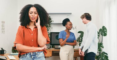 Bir kadın kollarını kavuşturup dinlerken diğerleri dedikodu yapıyor, kabadayılık taslıyor, dışlanıyor, bitkilerle parlayan çalışma alanı çağdaş bir iş ortamı yaratıyor..