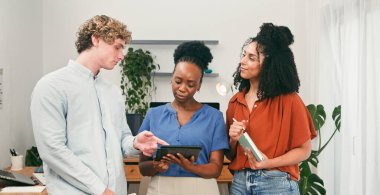 Üç farklı profesyonel, parlak ve modern bir ofiste, fikirleri tartışan, strateji planlayan ve bilgi paylaşan, takım çalışması, danışmanlık ve verimli bir çalışma alanında etkili bir iletişimi paylaşan bir tableti inceleyerek iş birliği yaparlar..