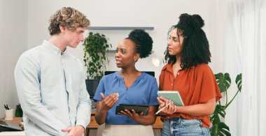 Çeşitli bir grup iş arkadaşı, birlikte bir proje planlamak için tablet ve defterler kullanarak, parlak, çağdaş bir ofiste sohbet ve işbirliği yapıyorlar..