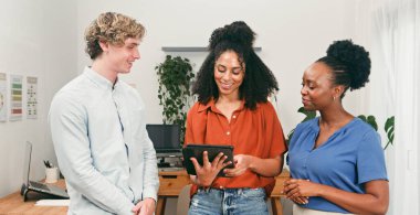 Üç farklı iş arkadaşı parlak bir ofiste dostça bir anı paylaşıyor, bir tabletteki bilgileri gözden geçiriyorlar. Sahne, takım çalışması, işbirliği ve pozitif çalışma kültürü taşır.