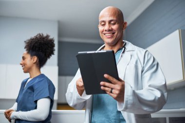 Elinde tablet olan gülümseyen bir doktor ve klinikte duran bir hemşireden oluşan bir tıbbi ekip, etkili bir şekilde işbirliği yapar. Profesyonel bir ortamda ileri teknolojiyi kullanarak sağlık hizmetleri çözümlerine girişiyorlar..