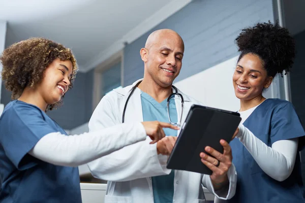 Sağlık çalışanlarından oluşan bir ekip, hasta bilgilerini tartışmak üzere bir tabletin etrafında toplandı. Grup, modern tıbbi uygulamalar ve sağlık ortamlarında takım çalışmasının önemini vurgulayarak takım çalışması ve işbirliği yayıyor..