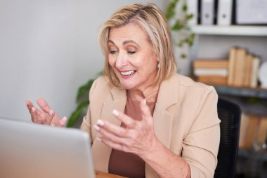 Bej rengi ceketli olgun bir kadın, bir masada oturuyor ve modern bir ofiste verimli bir iş görüşmesi yaparken dizüstü bilgisayara gülümsüyor ve el kol hareketi yapıyor..