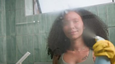 Genç, siyah, doğal saçlı bir kadın banyo bardağını özenle temizliyor. Bu basit hareket onun sabah rutininin bir parçası. Verimli ev bakımı ve temizliği gösteriyor..