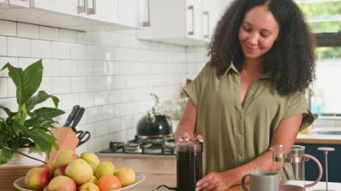 Mutlu bir kadın, parlak, modern mutfağında taze kahve çekirdeklerini öğütürken gülümser. Sabah içkisini hazırlar. Güne lezzetli bir ev yapımı içecekle başlamaya hazır bir Fransız makinesine zemin hazırlar..