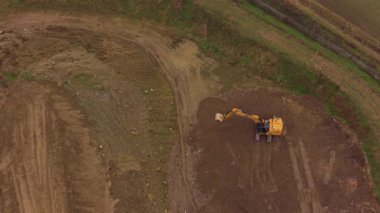 Sarı bir kazıcının yukarıdan aşağıya havadan görünüşü toprak kazıyor ve bir inşaat alanında toprağı hareket ettiriyor. Peyzaj üzerinde çalışan ağır makineler