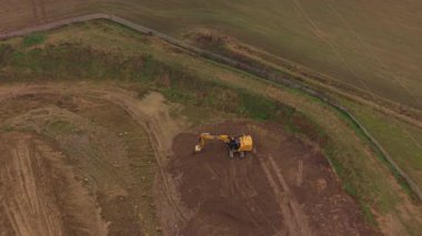 Sarı bir kazıcının toprağı kazma ve hareket ettirme görüntüsü. Ağır makineler büyük bir inşaat sahasının zeminini yıkıyor.