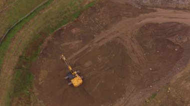 Sarı hidrolik kazıcının yüksek açılı insansız hava aracı görüntüsü toprağı kazıyor ve inşaat alanında yüklü miktarda bahşiş veren bir kamyona toprak yüklüyor.
