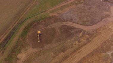 Güçlü bir sarı kazıcının yüksek açılı görüntüsü toprağı kazıyor ve bir inşaat alanında toprağı hareket ettiriyor. Ağır makineler toprak çalışması yapıyor