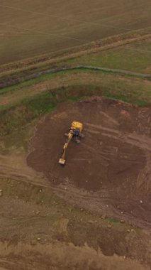 Yüksek açılı insansız hava aracı görüntüleri, sarı bir kazıcının bir inşaat alanında toprağı hareket ettirdiğini gösteriyor. Ağır makineler toprağı kazıyor ve düzleştiriyor.