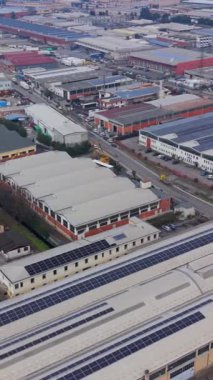 Geniş bir sanayi bölgesinde uçan yüksek açılı insansız hava aracı görüntüleri çatılarında güneş panelleri olan çok sayıda fabrika ve depo gösteriyor.