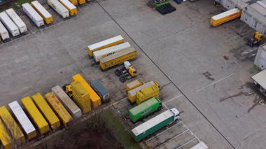 Bir kamyon şoförünün yoğun bir lojistik merkezinde römork park ederken yüksek açılı görüntüsü. Merkeze bir sürü renkli kargo karavanı park edilmiş.