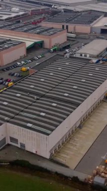 Yükleme limanları, park etmiş kamyonlar ve arabalarla dolu depoları olan büyük bir endüstriyel kompleksin yüksek açılı görüntüsü. Modern lojistik ve ticaret alanı