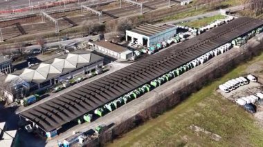 Demiryolu yakınlarındaki büyük bir tepe örtüsünün altında düzenli olarak park etmiş çok sayıda çöp kamyonu bulunan bir belediye atık yönetim deposunun hava perspektifi