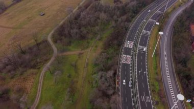 Arabaların ve kamyonların tepeden aşağı hava görüntüsü çok şeritli bir otoyolda ilerlerken kırsal bir alanda tarlalar ve ağaçlarla kıvrılıyor.
