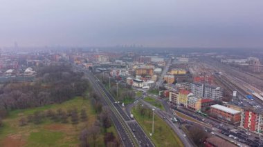 Trafiği ve kentsel gelişimi olan bir şehrin ortasından geçen büyük bir otoyolun yüksek açılı görüntüsü. Şehir manzarasının üzerinde sisli bir gökyüzü asılı.