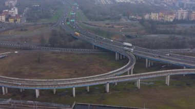 Bulutlu bir günde, karmaşık bir otoyol kavşağının yüksek açılı görüntüsü. Otoyolda giden araba ve kamyonlar, üstgeçitler ve rampalar.