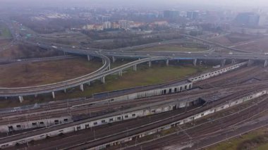 Karmaşık bir karayolu kavşağı ve birden fazla demiryolu hattını gösteren hava görüntüleri. Bulutlu bir günde binaların ve trafiğin olduğu şehir manzarası