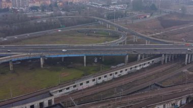 Karmaşık bir yol kavşağının havadan görüntüsü. Otoyol üst geçidinde giden arabalar ve kamyonlar. Altından geçen raylar.