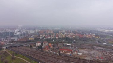 Geniş bir demiryolu ağı, şehir binaları ve otobanlar sisle kaplanmış, ulaşım ve şehir yaşamını gösteren kasvetli şehir manzarası