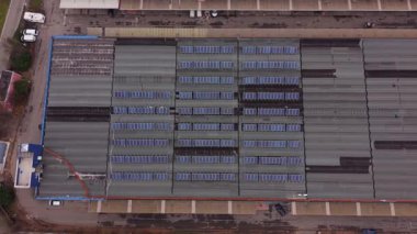 Bir endüstri binasının yüksek açılı yukarıdan aşağı manzarası sürdürülebilir ve yenilenebilir enerji için güneş panellerinden oluşan sıralarla kaplı.