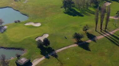 Güneşli bir günde yeşil golf sahasında kum tuzakları ve küçük bir göl olan yalnız bir insanın hava manzarası.