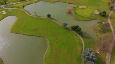 Göl ve kum tuzaklarıyla dolu güzel yeşil bir golf sahasının havadan drone görüntüsü. Tanınmayan insanlar rahatlatıcı bir oyun oynuyorlar.