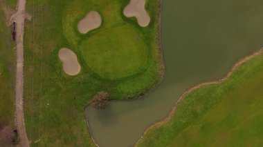 Sersemletici tepeden tırnağa yemyeşil golf sahası manzarası, kum sığınakları ve sakin bir su tehlikesi, mükemmel bir elit spor geçmişi.